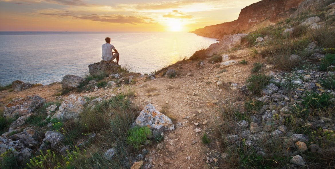 Man sitting on the rock cliff in mountain and watching on thr sunrise sea. Nature composition.