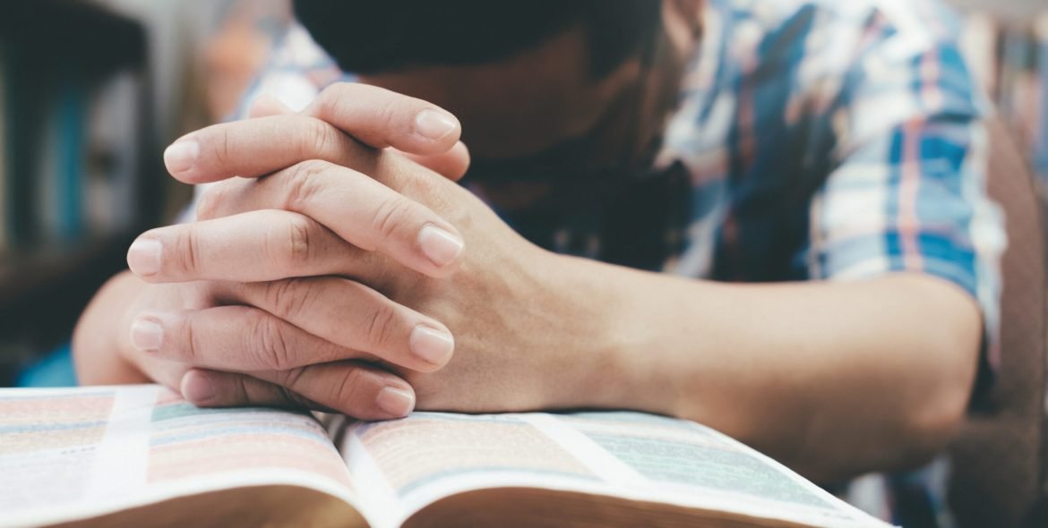 Religion, Christianity, Praying.  Man praying, hands clasped together on her Bible.
