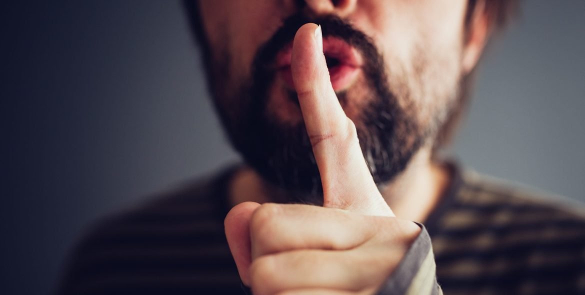 Man saying hush or be quiet with finger on lips, close up with selective focus