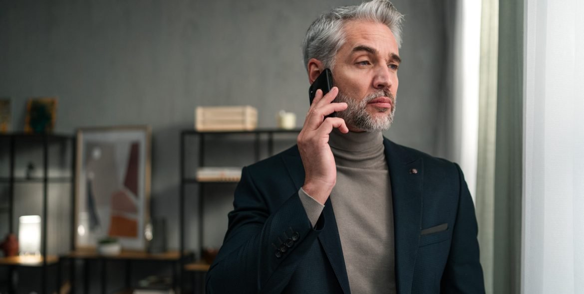 A mature businessman making a phone call indoors in office, looking away.