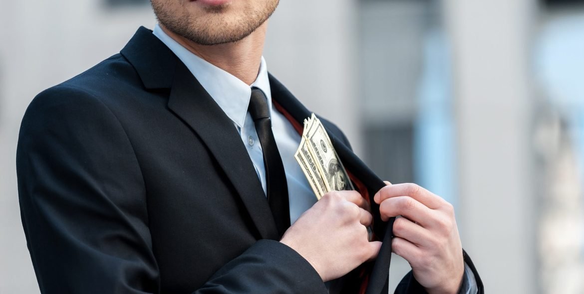 Pocketing company money. Cropped shot of a businessman placing money into his pocket