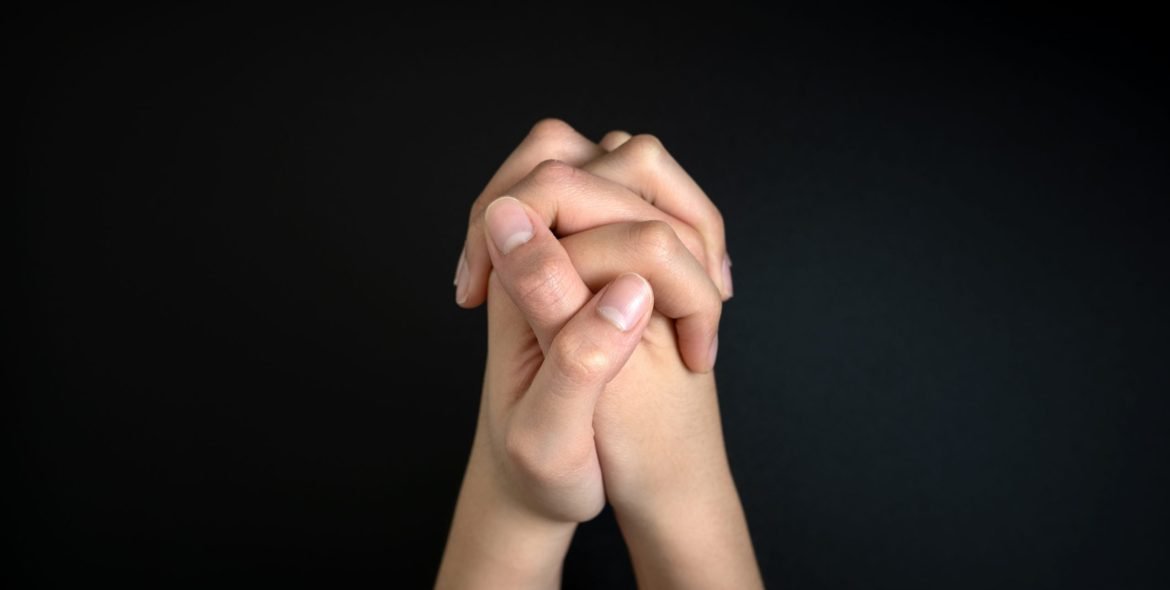 Praying hands is in the dark with light on the hands.