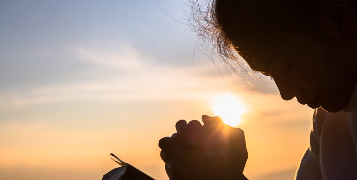 Silhouette of christian young woman praying with a  cross and open the bible at sunrise, Christian Religion concept background.