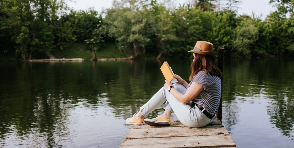 Young woman on the river pier reading book