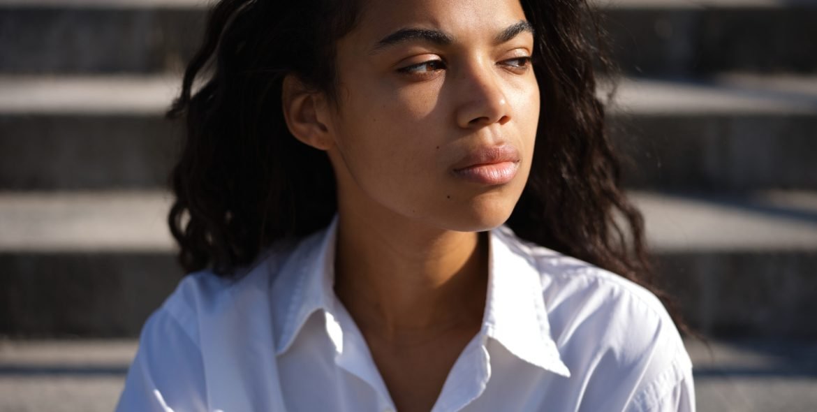 Resentment. Portrait of beautiful young mixed race woman in casual white shirt looking thoughtful aside while posing outdoors on a warm sunny day. Selective focus. Medium format shot
