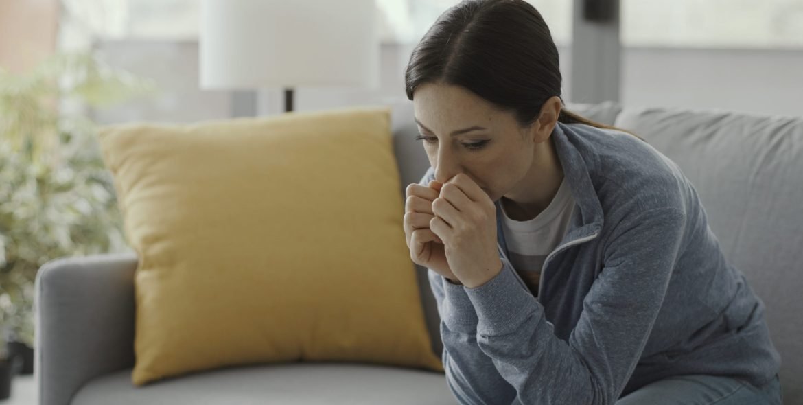 Sad depressed woman sitting on the couch self-isolating at home