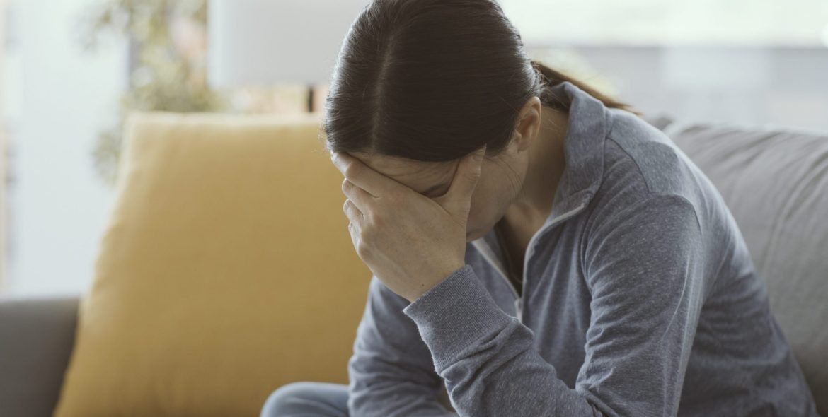 Sad depressed woman sitting on the couch self-isolating at home