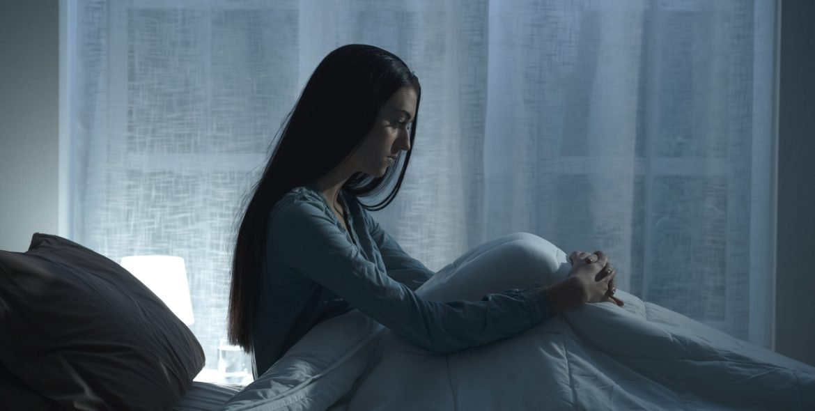 Sad depressed woman lying in bed late at night, she is suffering from insomnia and feels exhausted