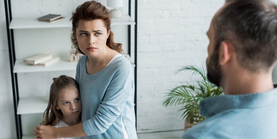 selective focus of scared mother hugging daughter and looking at husband
