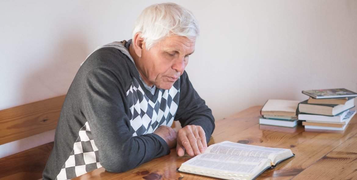 senior man praying, reading an old Bible. Hands folded in prayer on a Holy Bible in church concept for faith, spirituality and religion