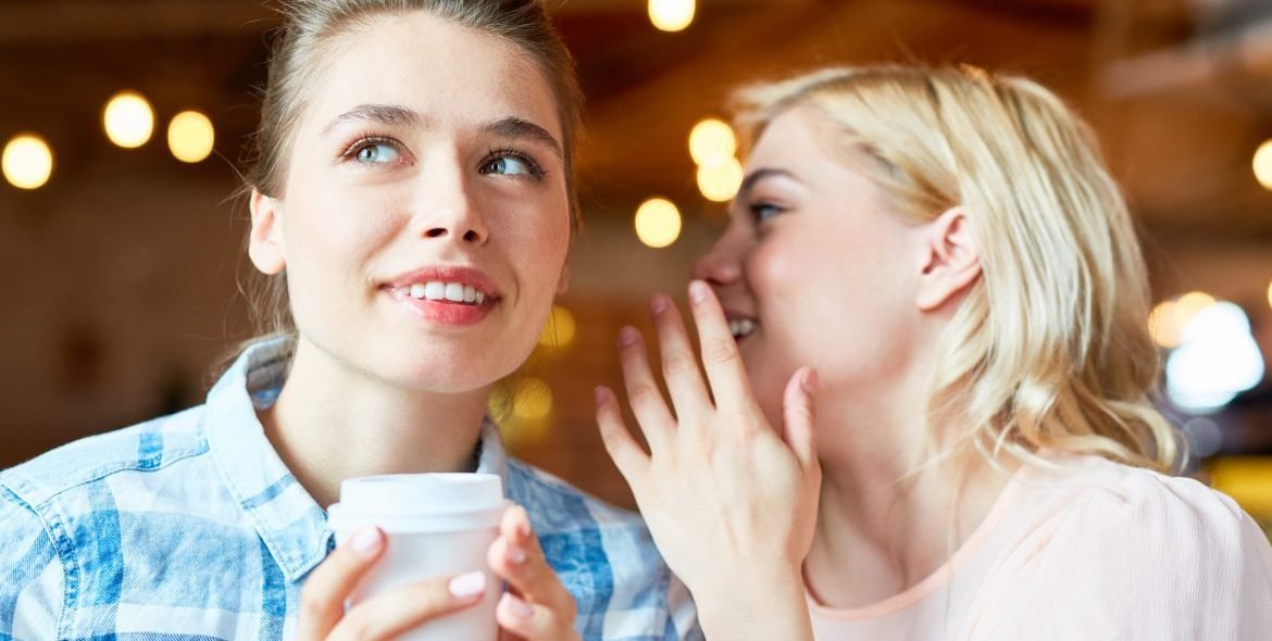 Young blonde whispering curious news in her friend ear at coffee break
