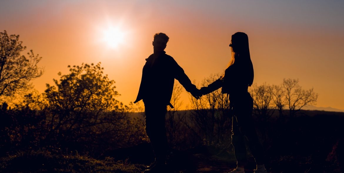 Silhouette of couple holding hands at sunset