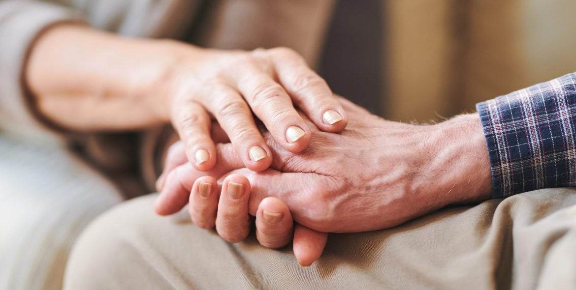 Senior male han between those of his mature wife or caregiver as symbol of support, care and love