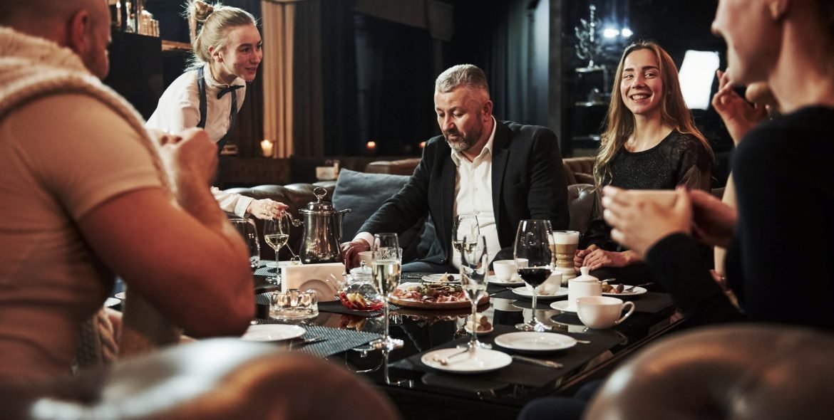 Talking with female waiter. Family friends having nice time in beautiful luxury modern restaurant.