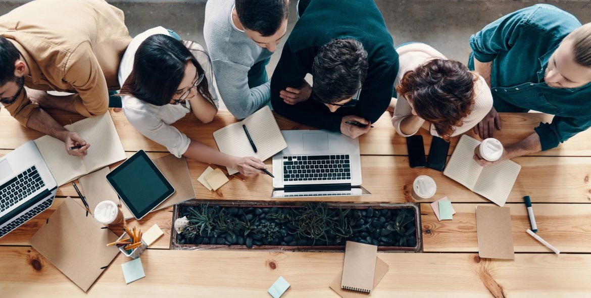 Teamwork. Top view of young modern people in smart casual wear using modern technologies while working in the creative office