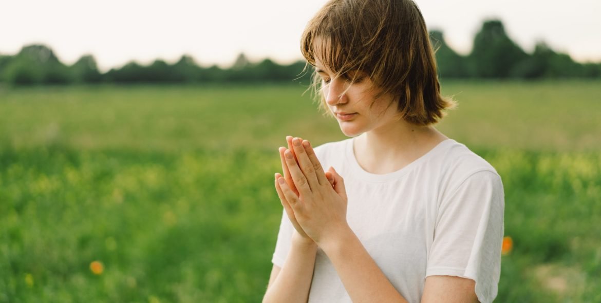 Teenager Girl closed her eyes, praying. Hands folded in prayer concept for faith, spirituality and religion. Peace, hope, dreams concept