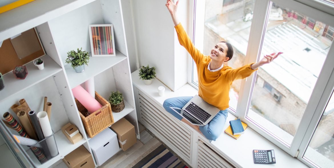 Happy young grateful businesswoman with laptop stretching her arms up while expressing triumph