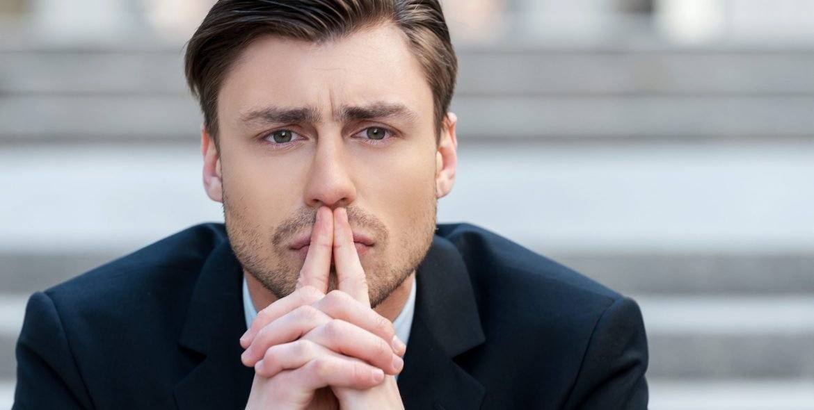 Thinking about solutions. Portrait of  young man in formalwear holding hands clasped and looking away while sitting outdoors