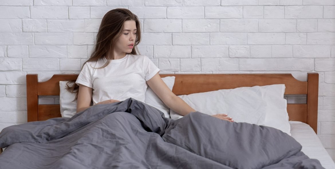 Unhappy young woman lost in sad memories, remembering her deceased husband, stroking his pillow on bed at home, copy space. Widow feeling lonely and depressed, suffering from loss of beloved man