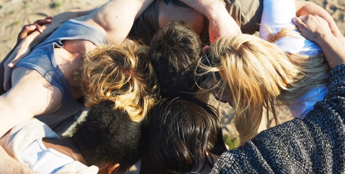 Top view of five friends leaning their heads and making circle over sand