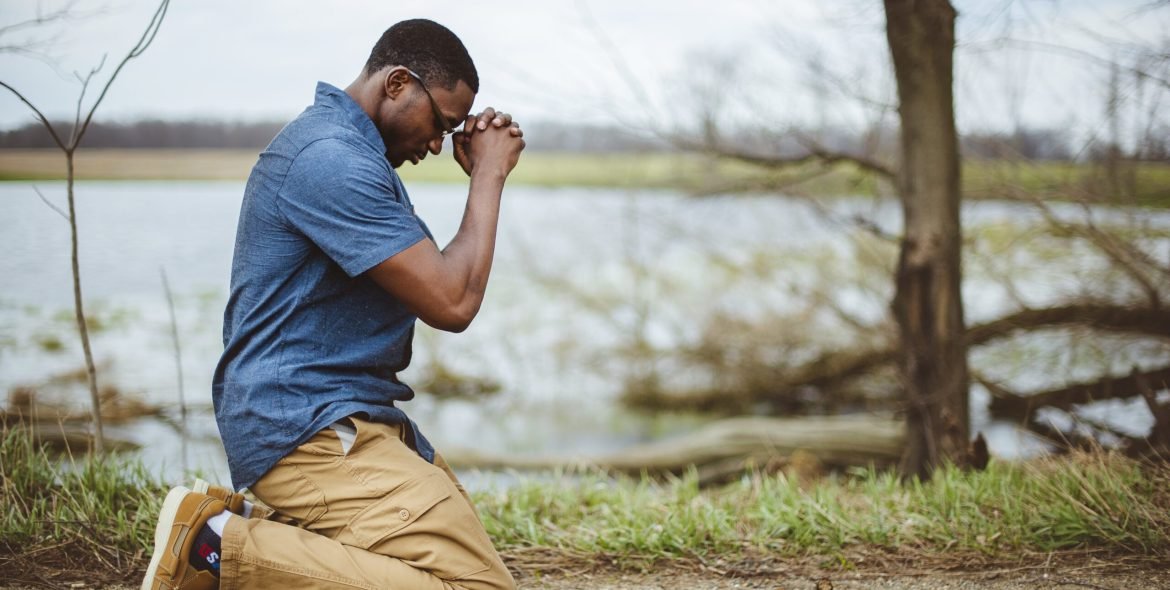 A vertical shot of an African-American male praying on his knees