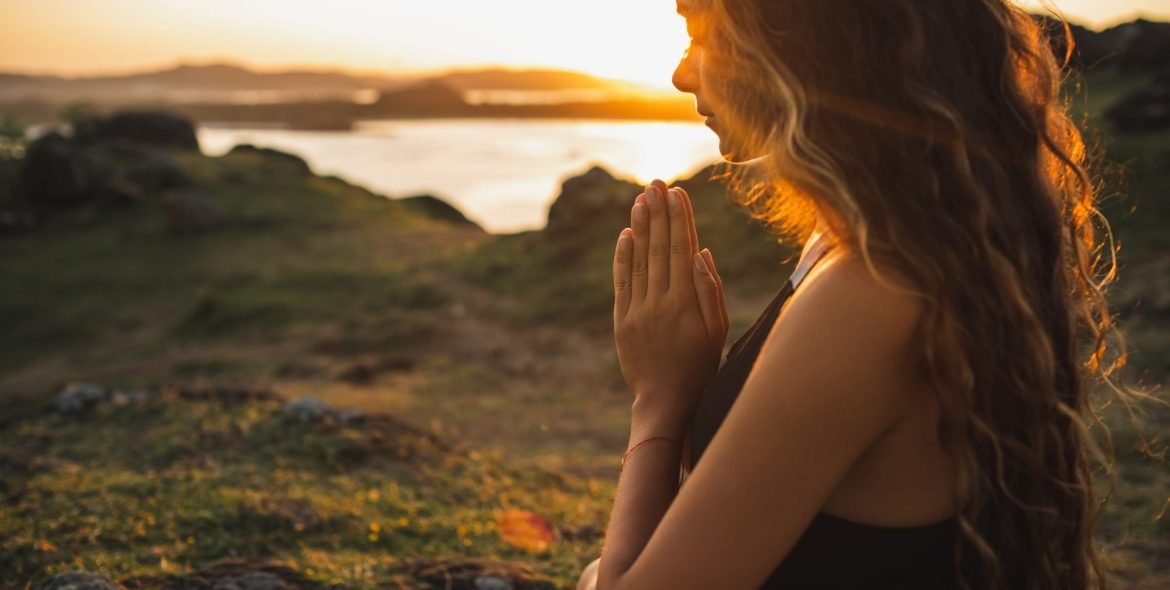 Woman praying alone at sunrise. Nature background. Spiritual and emotional concept. Sensitivity to nature