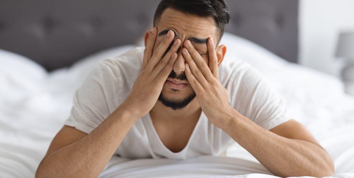 Young Arab Man Waking Up In Bed, Rubbing Eyes After Sleepless Night, Stressed Middle Eastern Guy Suffering From Insomnia Or Headache While Lying In Bedroom At Home, Closeup Shot With Free Space