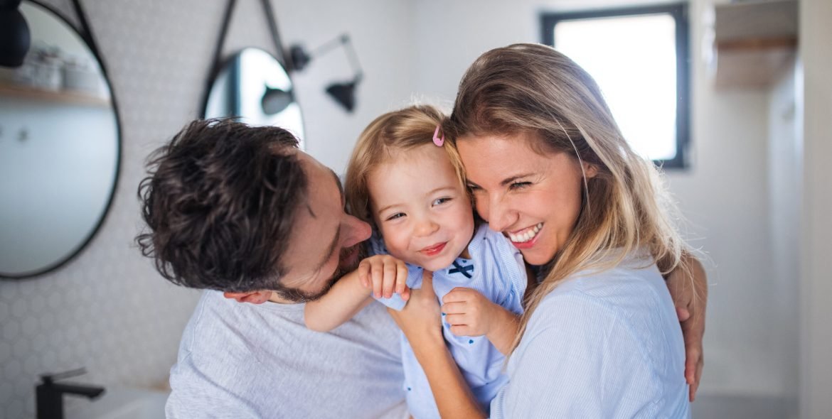 A young family with small daughter indoors in bathroom, hugging.