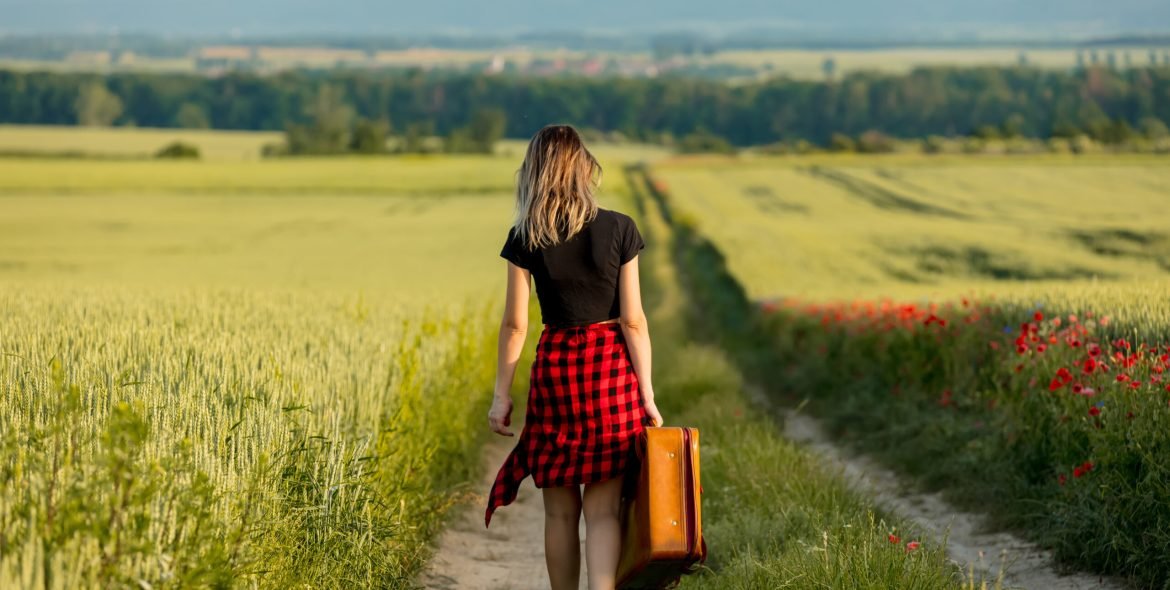 Young girl with suitcase walking down the road on countryside