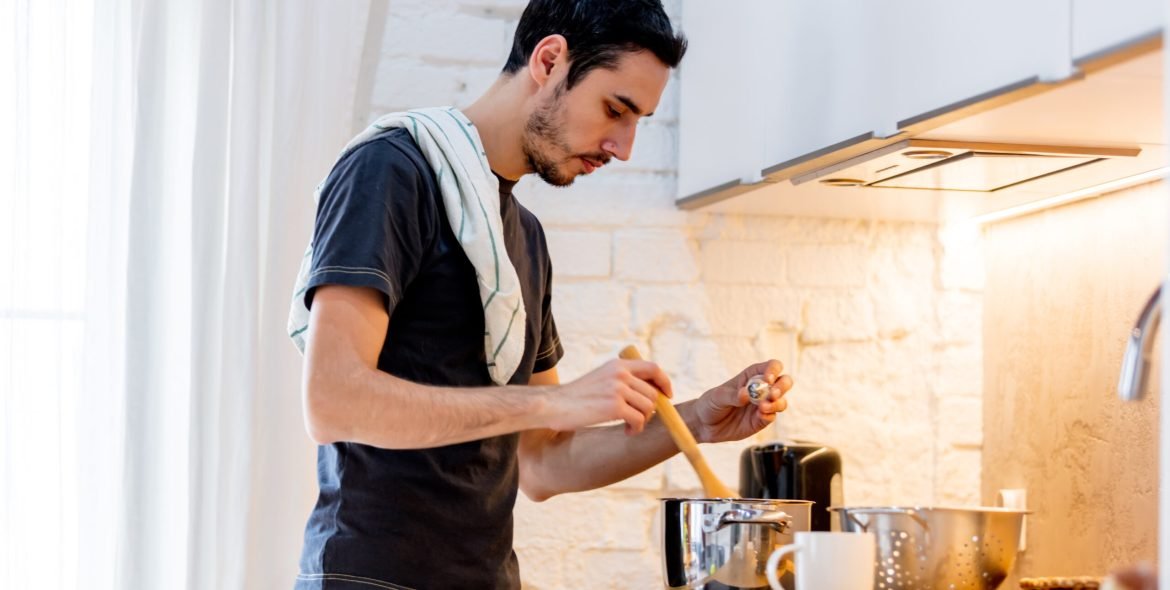 Young man in black shirt cooking at kitchen in home. candid view